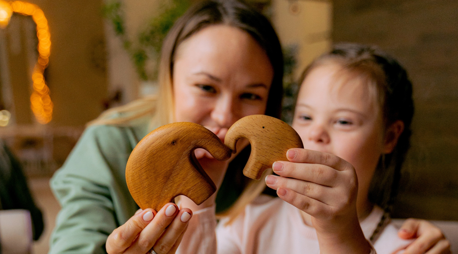 An early years educator playing with wooden elephants with a little girl