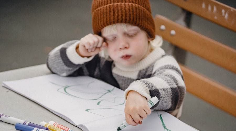 blonde child in brown hat drawing with green pen