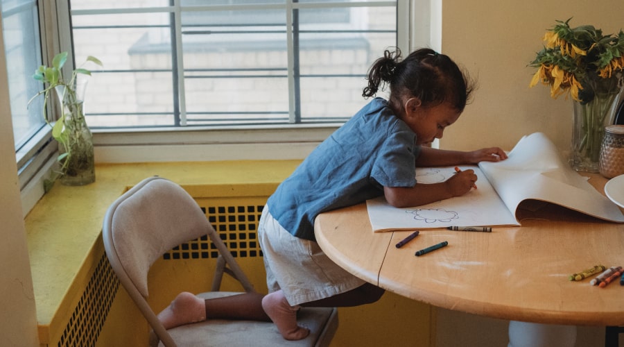child leaning over table colouring with crayons