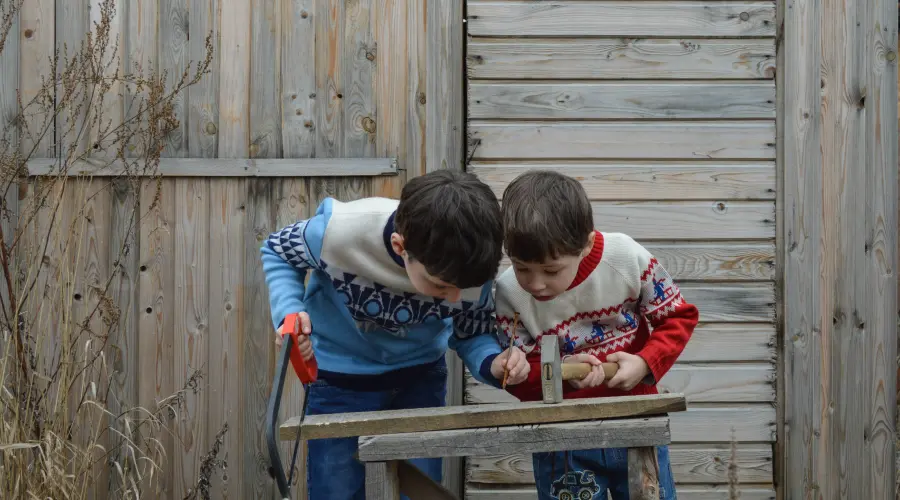 Two preschoolers share some woodworking tools, in a nursery garden.