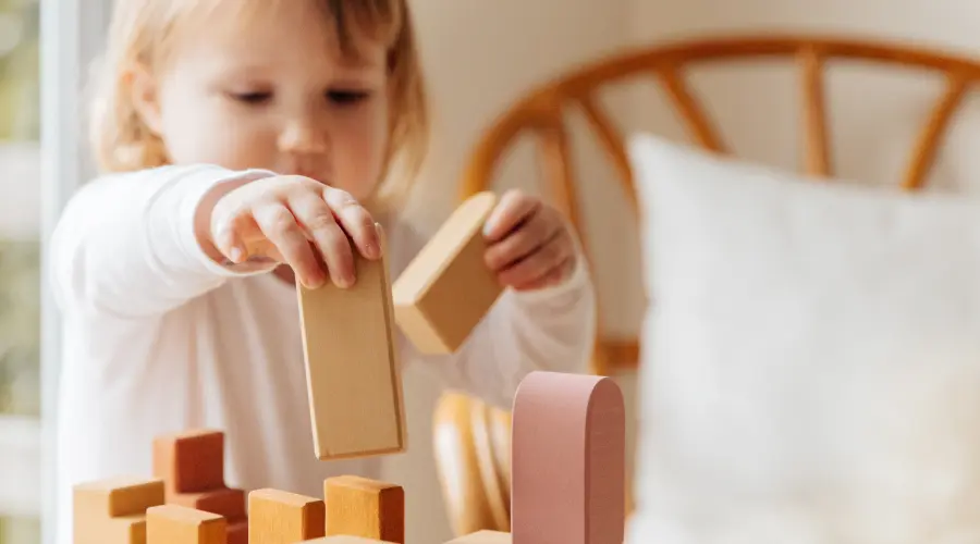 A toddler stacks some neutral-coloured wooden blocks