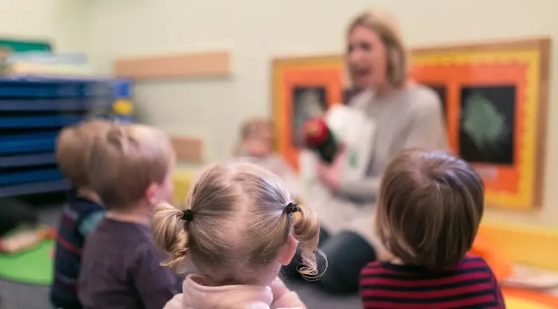 Teacher in a class with 4 kids sitting on the ground