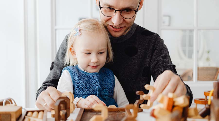 A photo of an Earl Years educator playing with wooden toys with a little girl. They are sitting at a table.