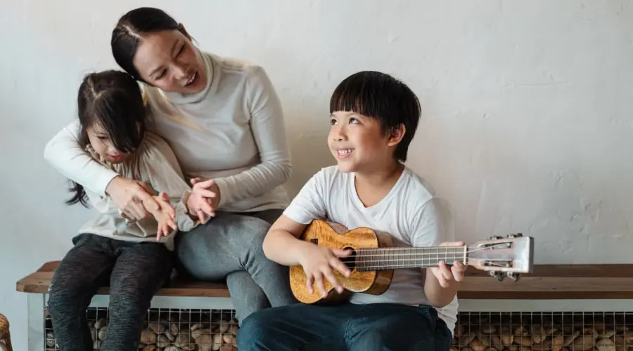 Boy playing ukulele, singing with his mother and sister