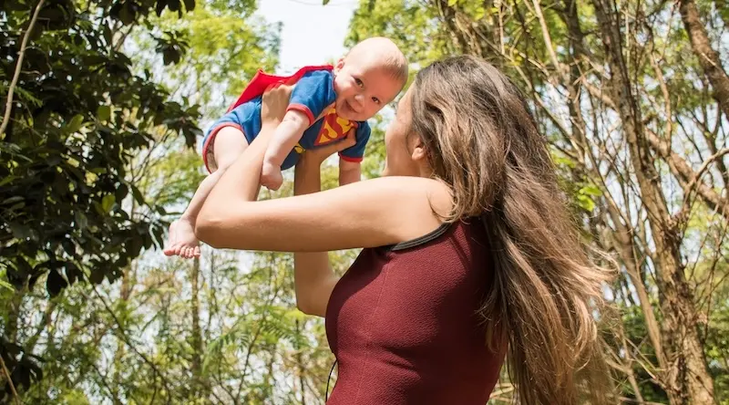Woman holding a baby in Superman costume in the air