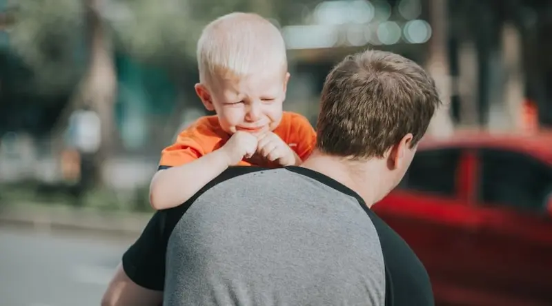 A crying child being held by an adult.