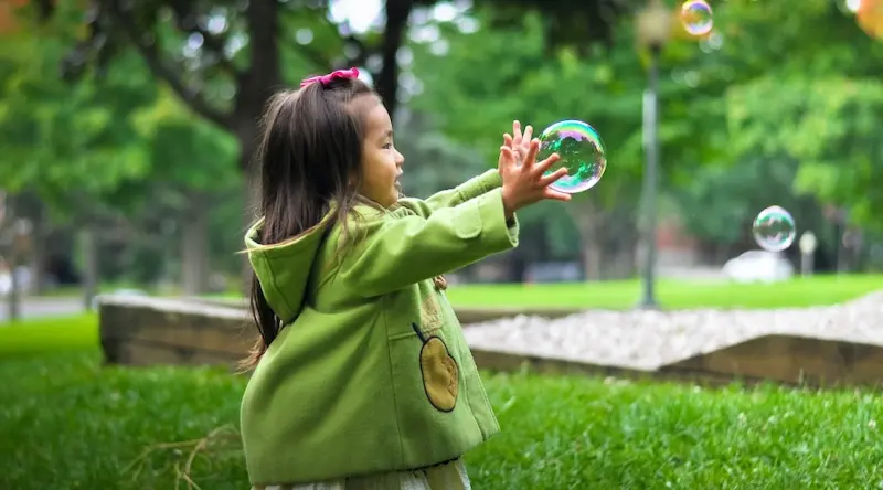 Little girl in green jacket playing with bubbles outdoors