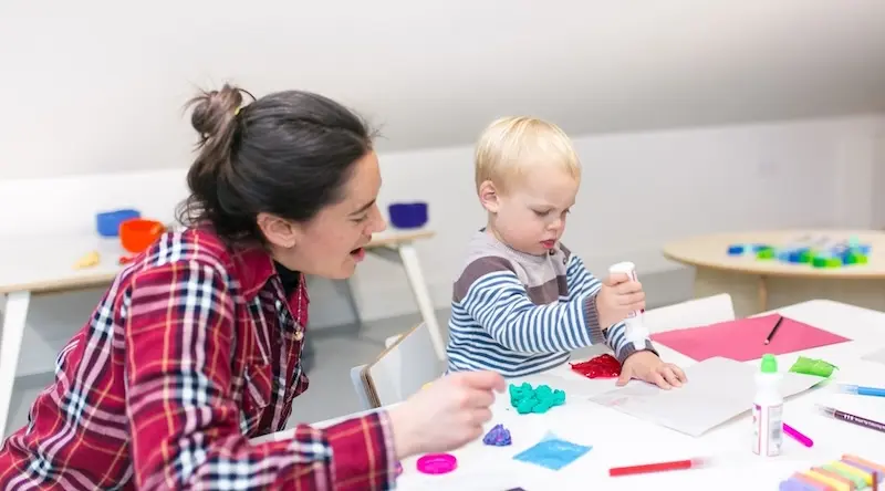 Teacher helping a little boy draw in a nursery