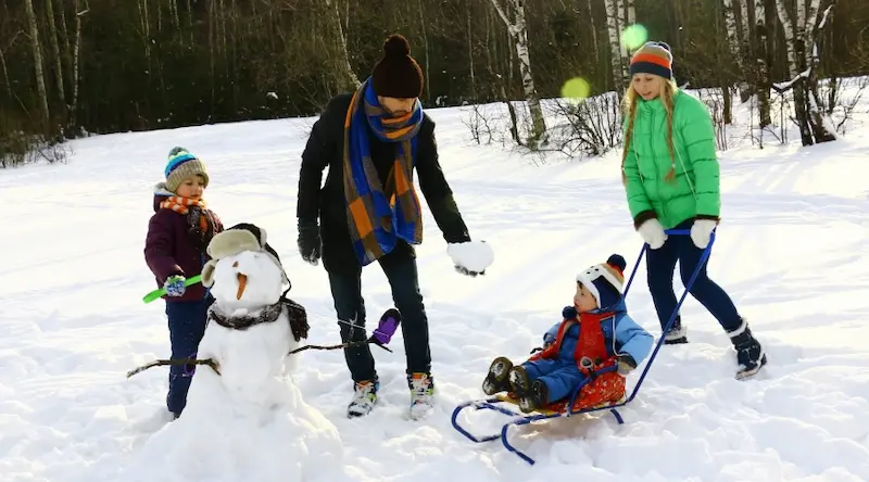 Famly of 4 playing outdoors in the snow building a snow figure