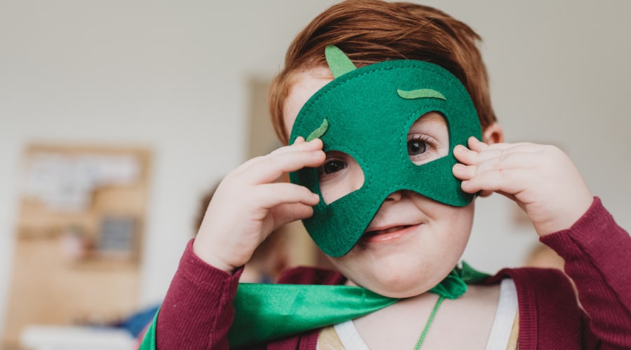 A young child wears a green mask and green cape