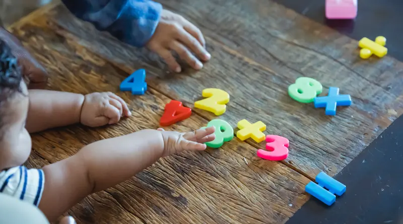 A baby playing with plastic numbers on a wooden desk.