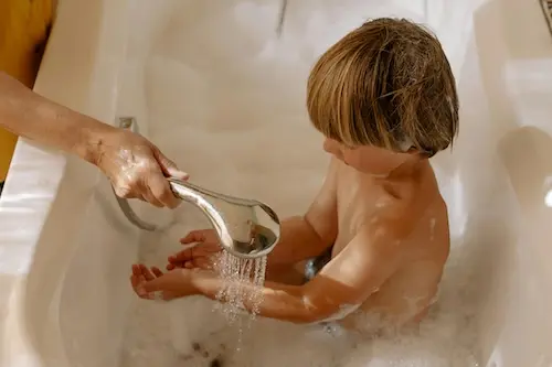 A parent supports an early ears child to explore water in the bath