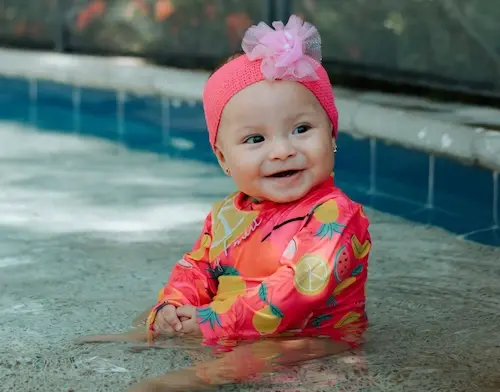 An early ears child in a bright rash vest, sitting in a paddling pool.