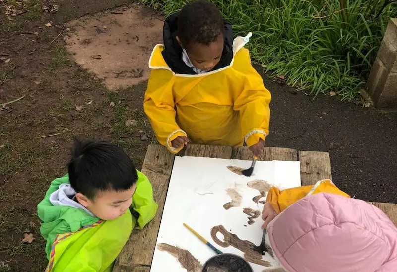 3 children from Acorns Preschool enjoy painting outside