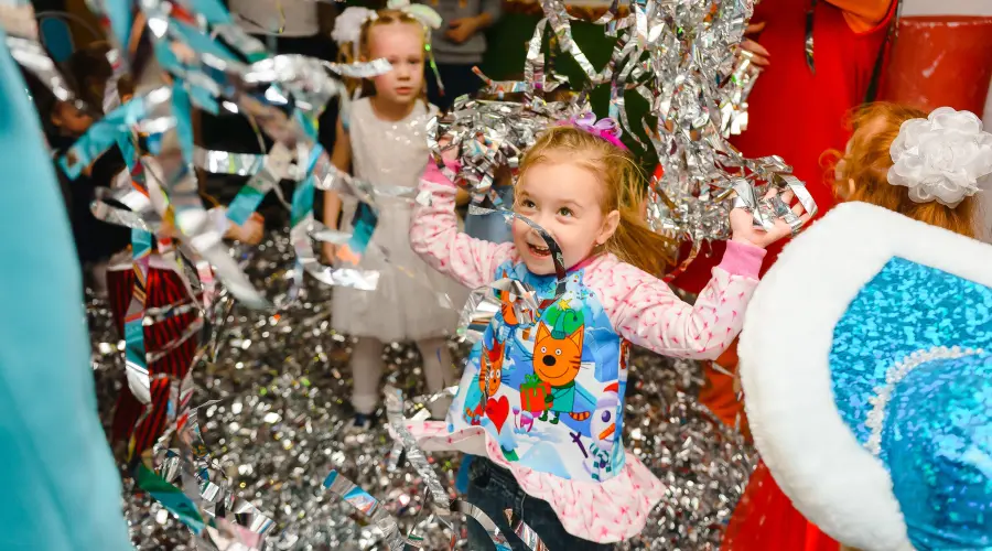 Two little girls dance amongst silver streamers at a nursery party.