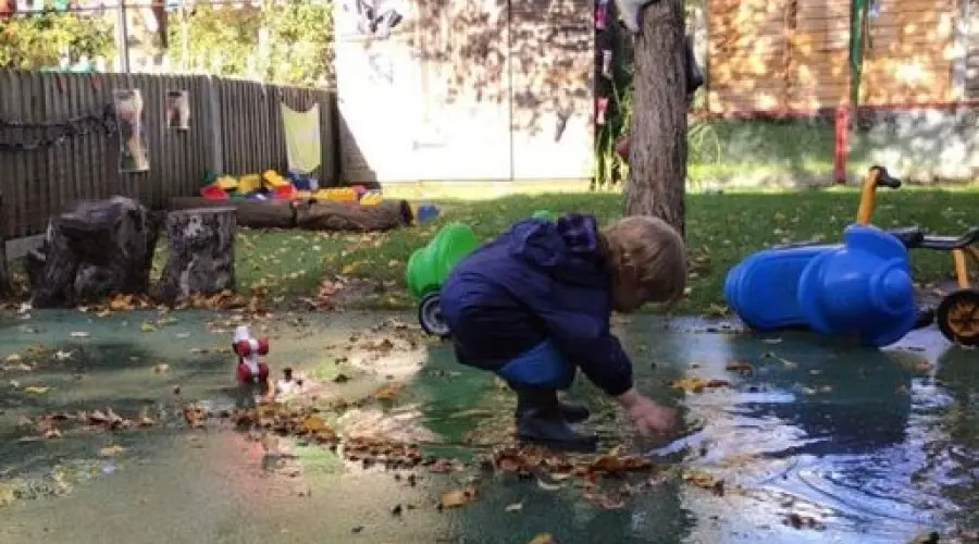 A photograph of a child playing in a puddle in the garden at Storkway Neighbourhood Nursery