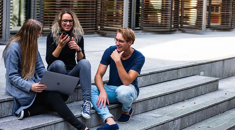 Three Early Years apprentices talk together while sitting on the steps outside a college.