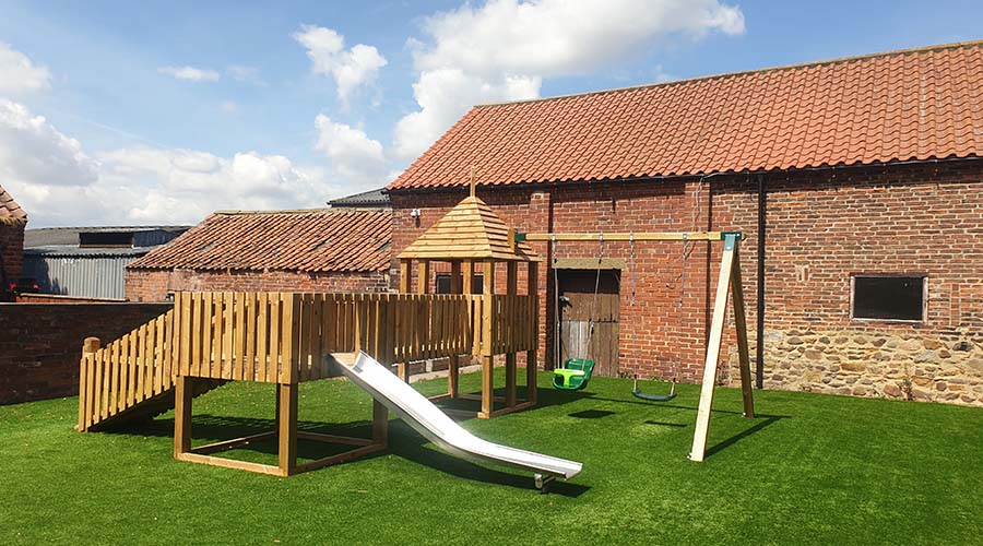 A wooden climbing frame in the garden of Goutlon Grange, with a slide, swingset, and a tower.