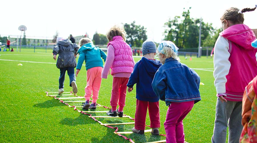 A group of Early Years children playing outside on a flat ladder obstacle.