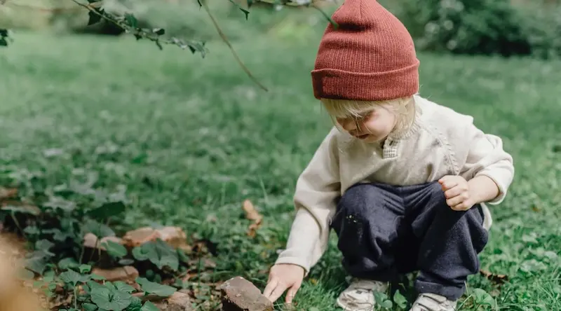 Child playing outdoors wearing a red hat