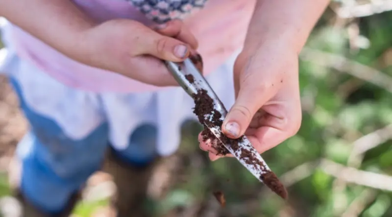 Child cleaning a knife rom dirt outdoors