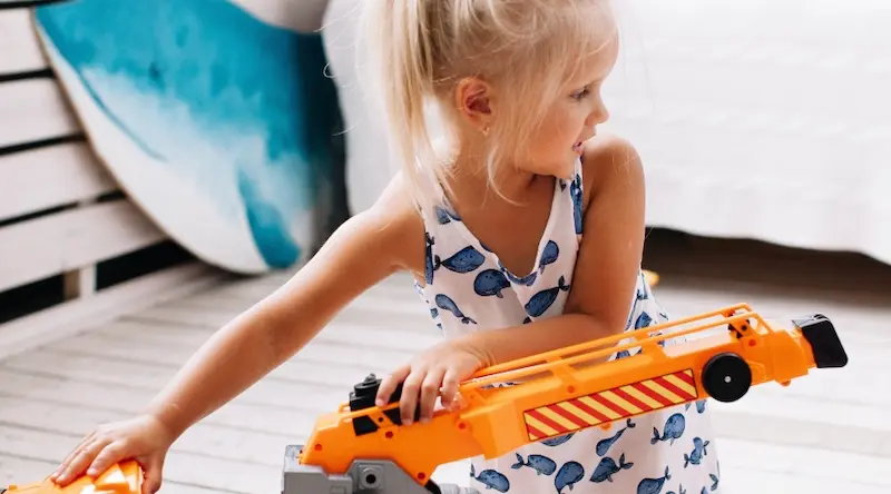 Little blond girl in a white dress with whales plays with a track toy