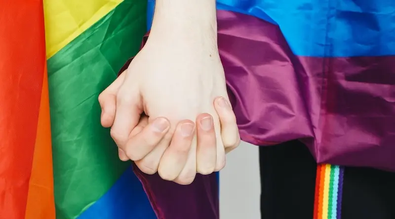 Two people holding hands in front of a rainbow flag