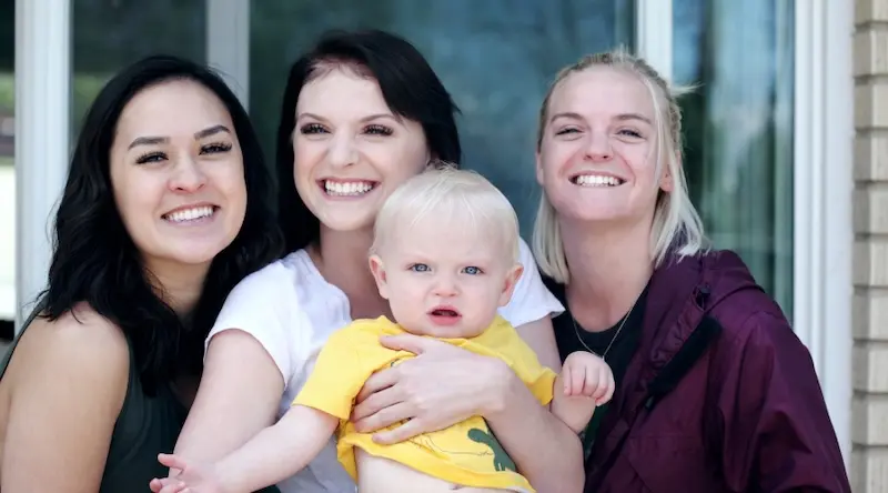 3 women pose for a picture with a toddler, all smiling