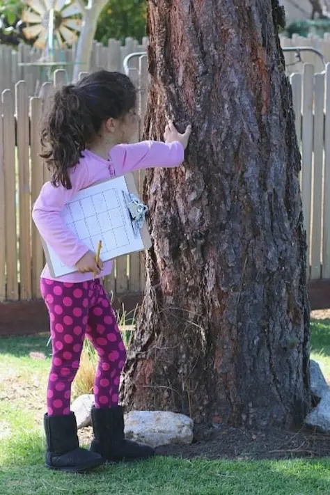 girl leaning on a tree holding paper and pen playing outdoor scavenger hunt