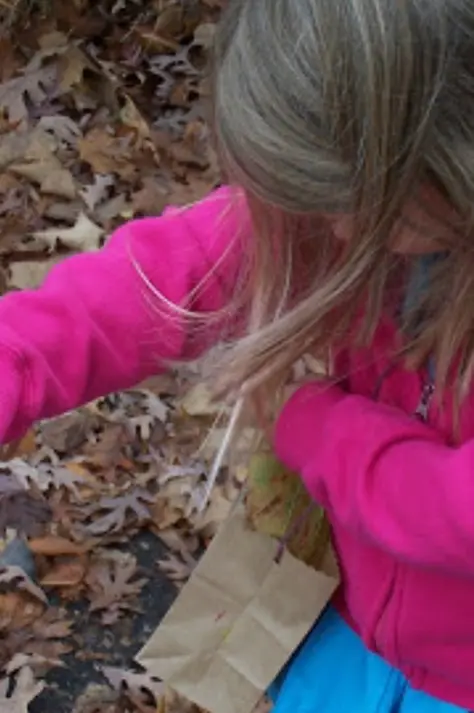 girl wearing pink collecting leaves in a paper bag