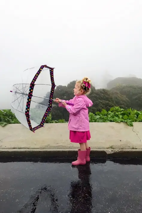 girl with rubber boots and umbrella playing in the rain