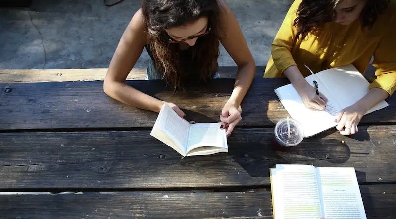 Two women writing and reading on a bench outside