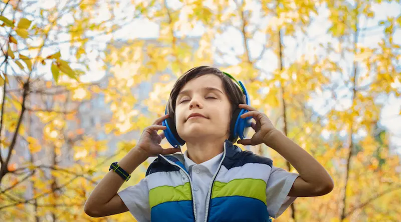 Child with headphones in the middle of yellow-leaves forest