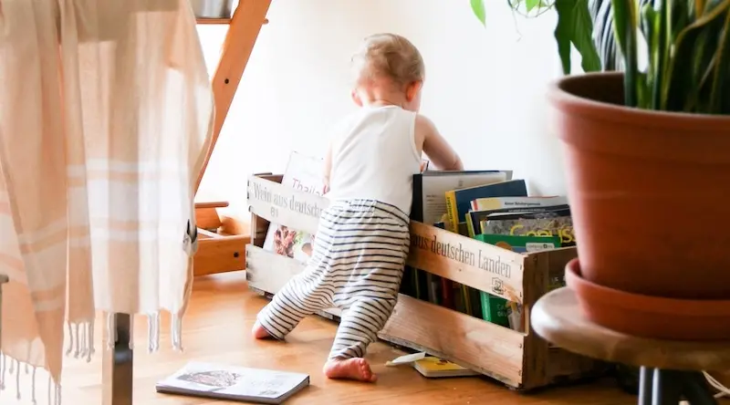 A toddler leans into a wooden box of books
