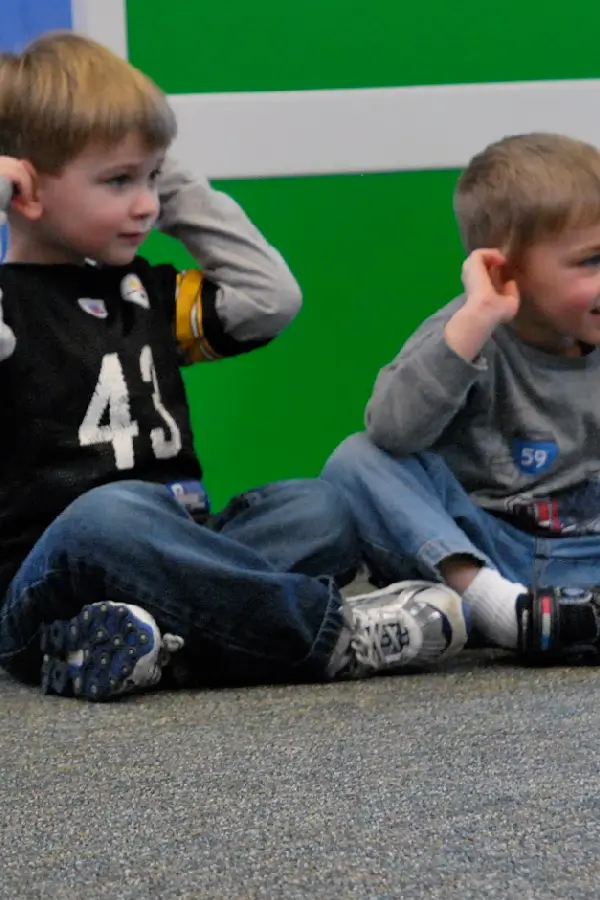 Two boys sitting on the ground with hands on ears