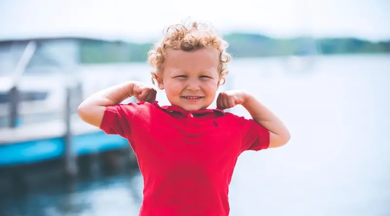 Boy in red t-shirt flexing by waterfront