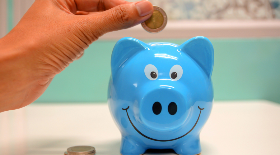 A person's hand putting a coin into a piggy bank