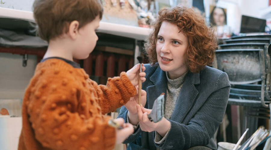 a preschool teacher helping a boy paint