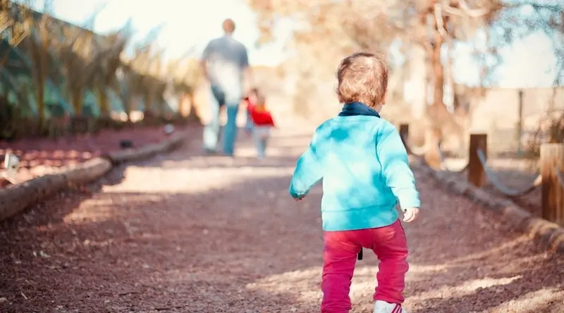 toddler in red trousers walking towards parent