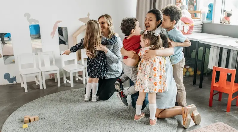 children and teachers at preschool or daycare hugging