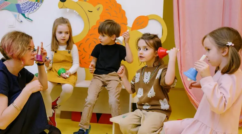 teacher and four kids playing with musical instruments at childcare or preschool