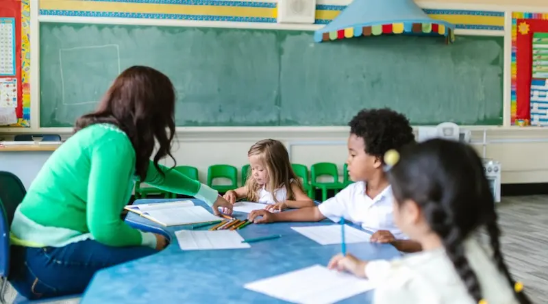 a teacher and three students in a preschool classroom