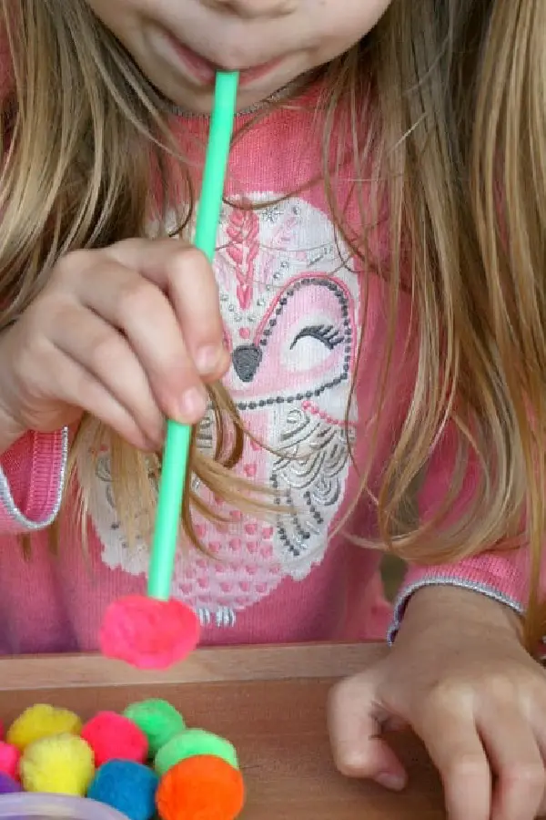 Small girl playing with a straw and pom poms