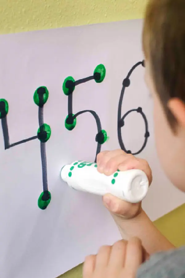A boy playing with a green marker drawing numbers