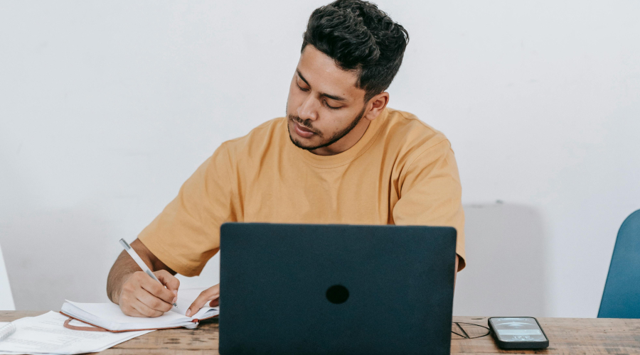 man at a table on his laptop and looking at his notepad