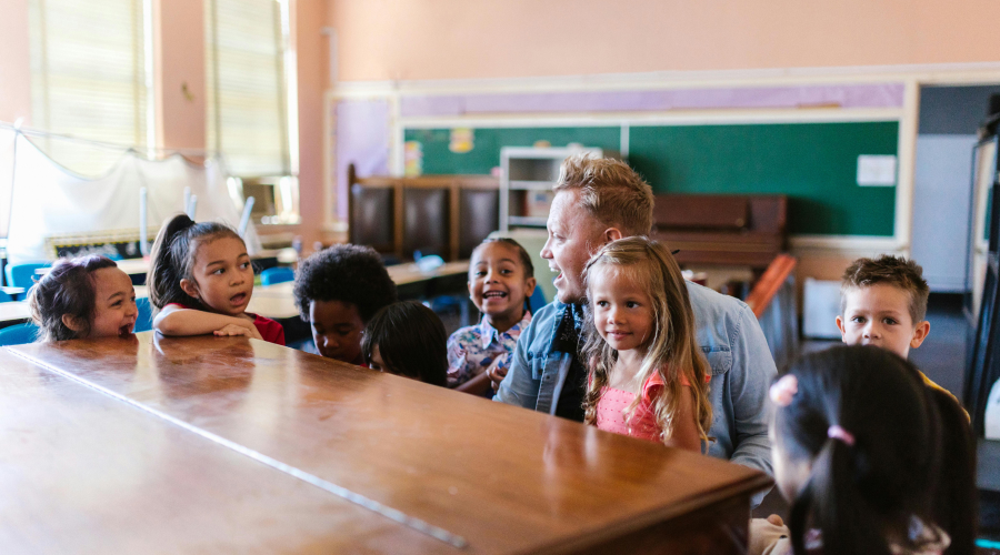 young kids and their teachers in the classroom sitting at a piano