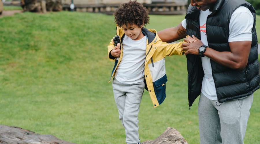 Man supporting a boy to stand on a rock