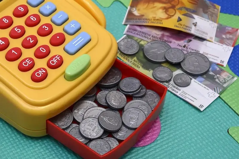A yellow toy cash register with some play money beside it