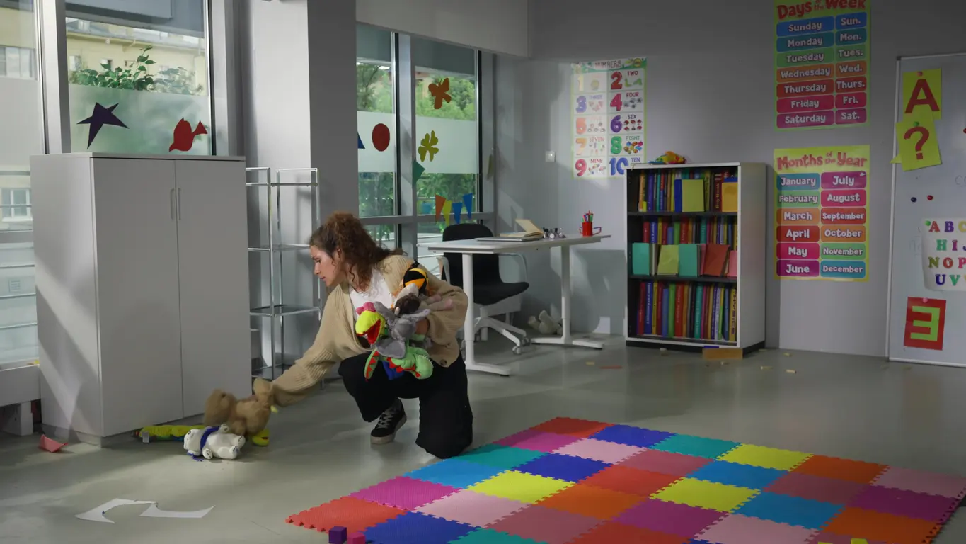 A centre worker picking up toys in an empty nursery room
