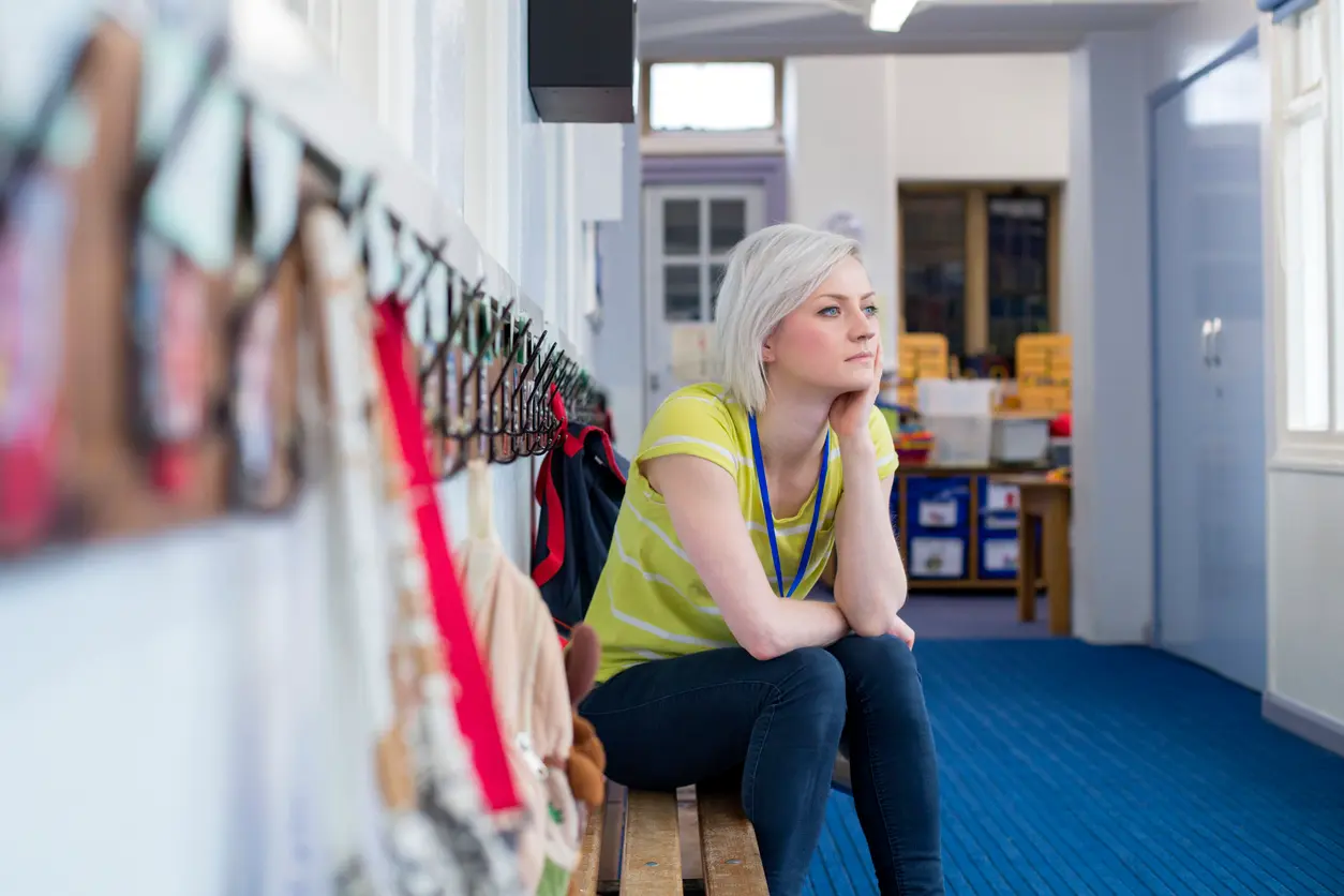 A blond young lady sitting thoughtfully on a bench in a nursery entrance